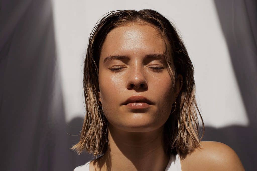 A woman faces into the sun with clear and healthy skin.