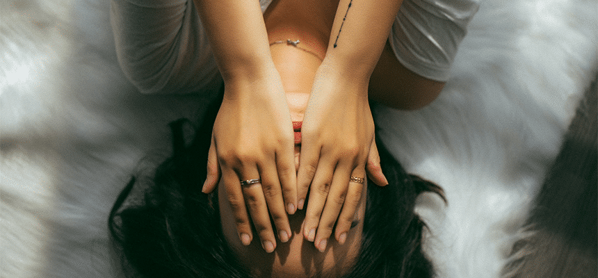 A photo of a visibly stressed young woman holding her hands to her face after not sleeping properly
