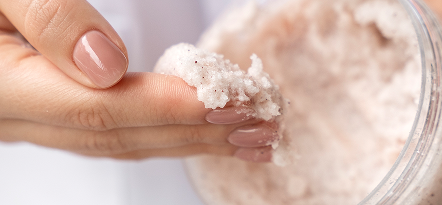 A hand reaching into a tub of exfoliating scrub with product on their fingers