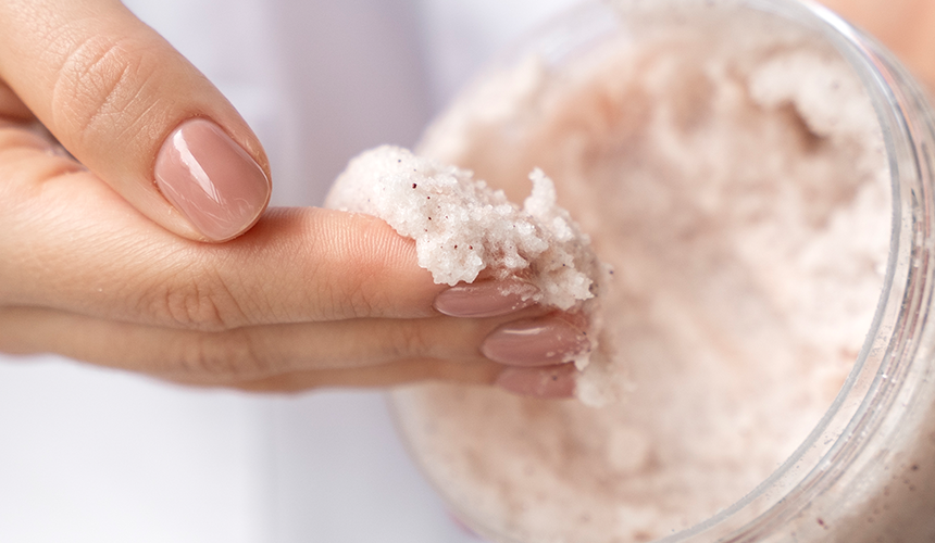 A hand reaching into a tub of exfoliating scrub with product on their fingers