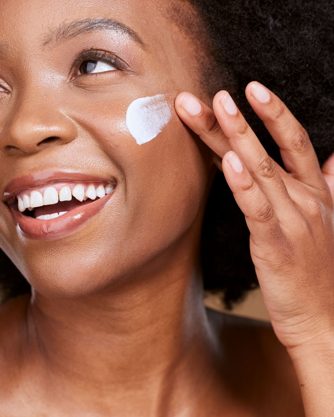 black woman smiling applying face cream