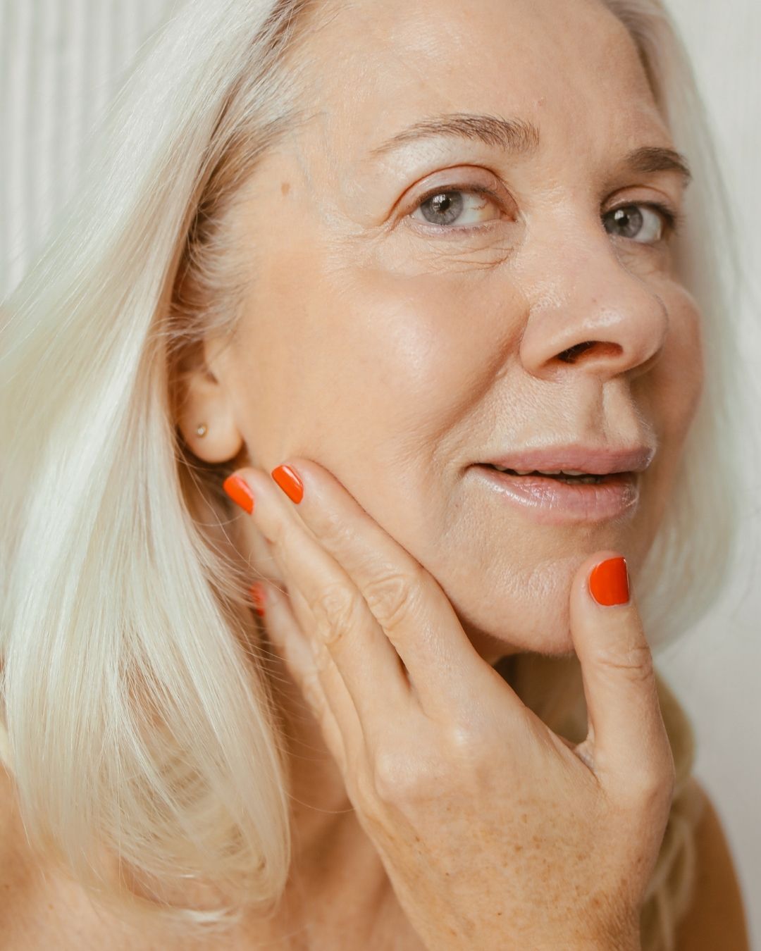 older white woman grey eyes white hair applying face serum