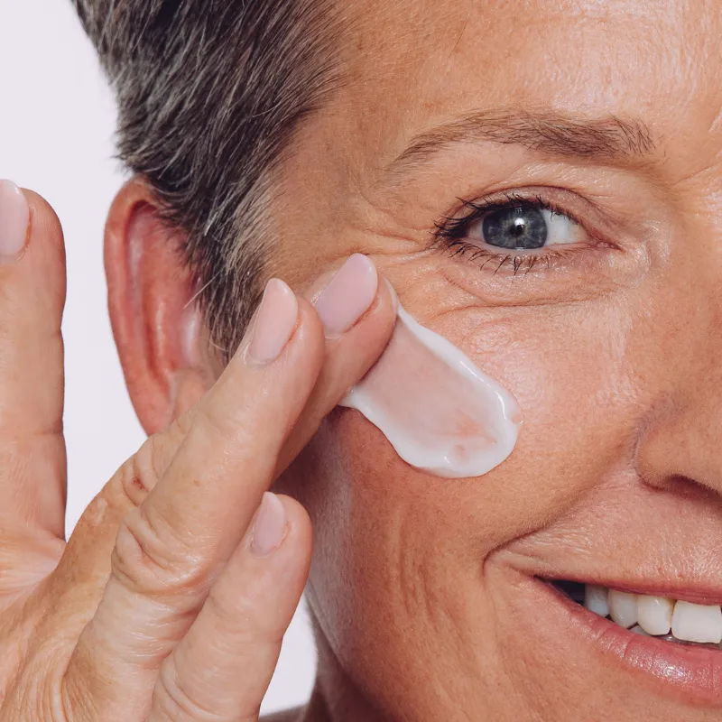 Close-up of Collagen Restore cream being applied onto glowing skin beside the eye and cheek area.